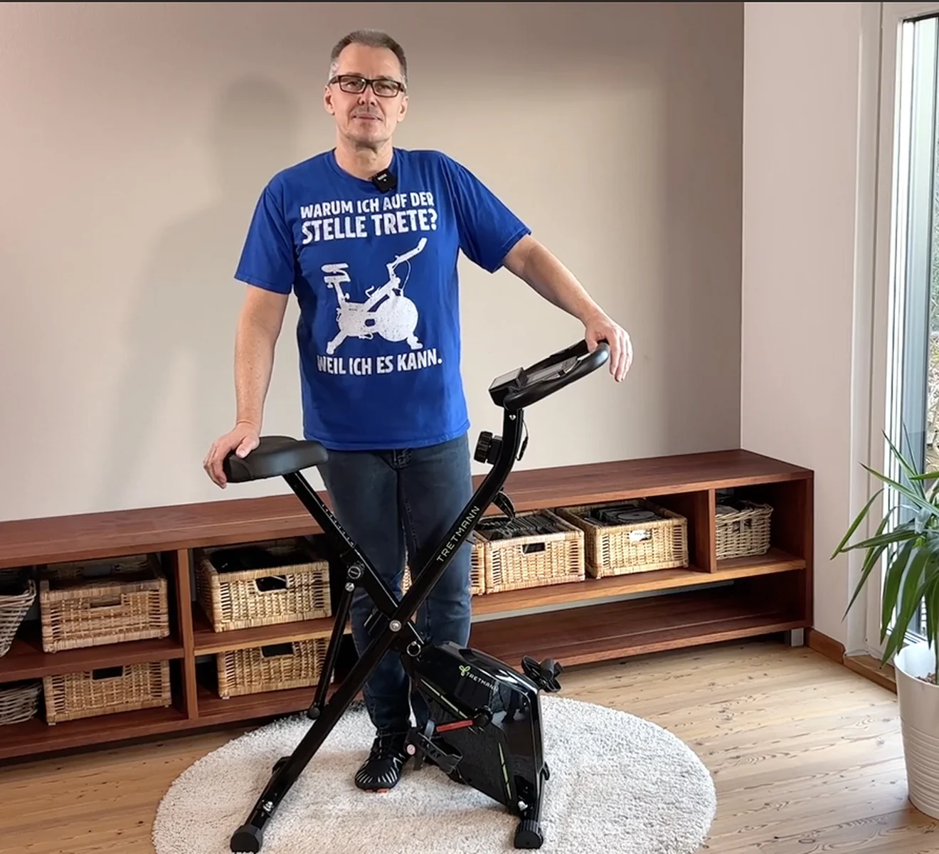 Mann über 50 steht neben seinem Tretmann Home im hellen Wohnzimmer
